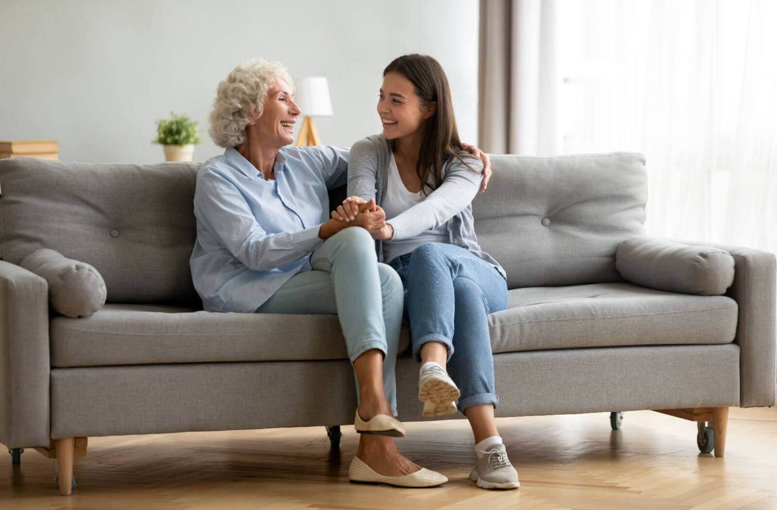 An older adult with dementia sitting on the couch, laughing and holding hands with their grandchild during a conversation.