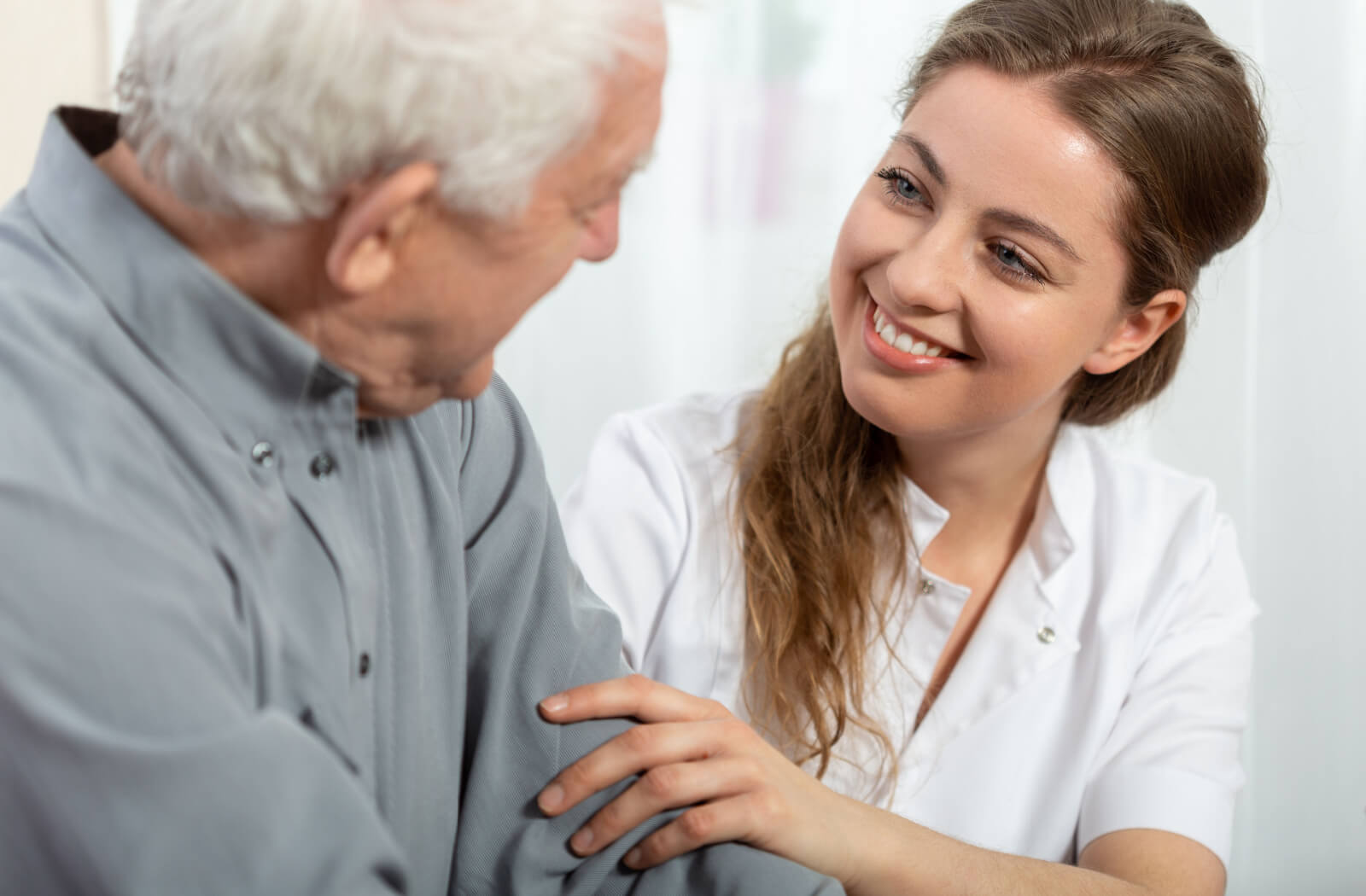 A young adult touching the arm of an older loved one with dementia while talking and smiling.