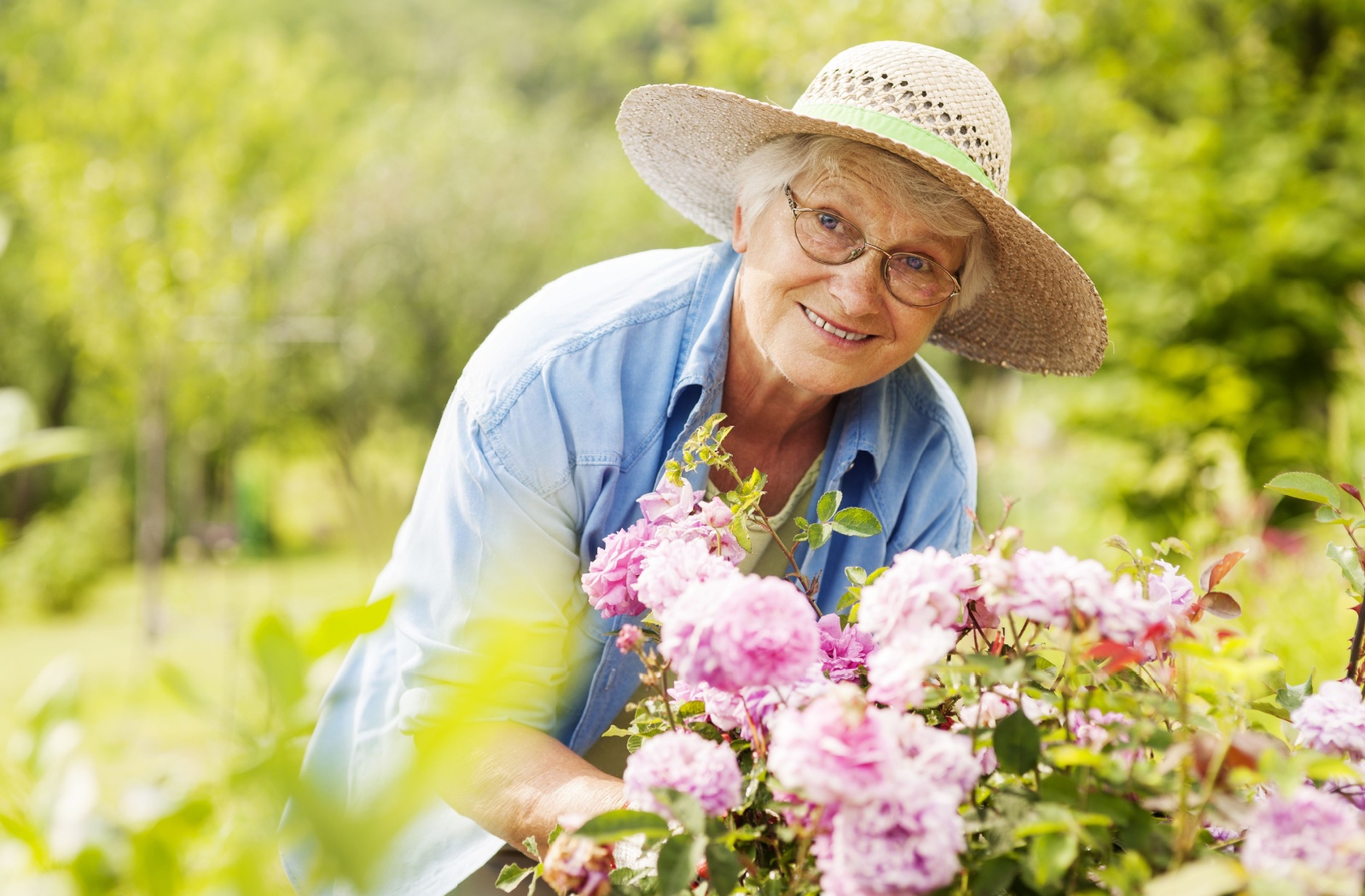 An older adult in a sunhat smiling while working in their own flower garden.