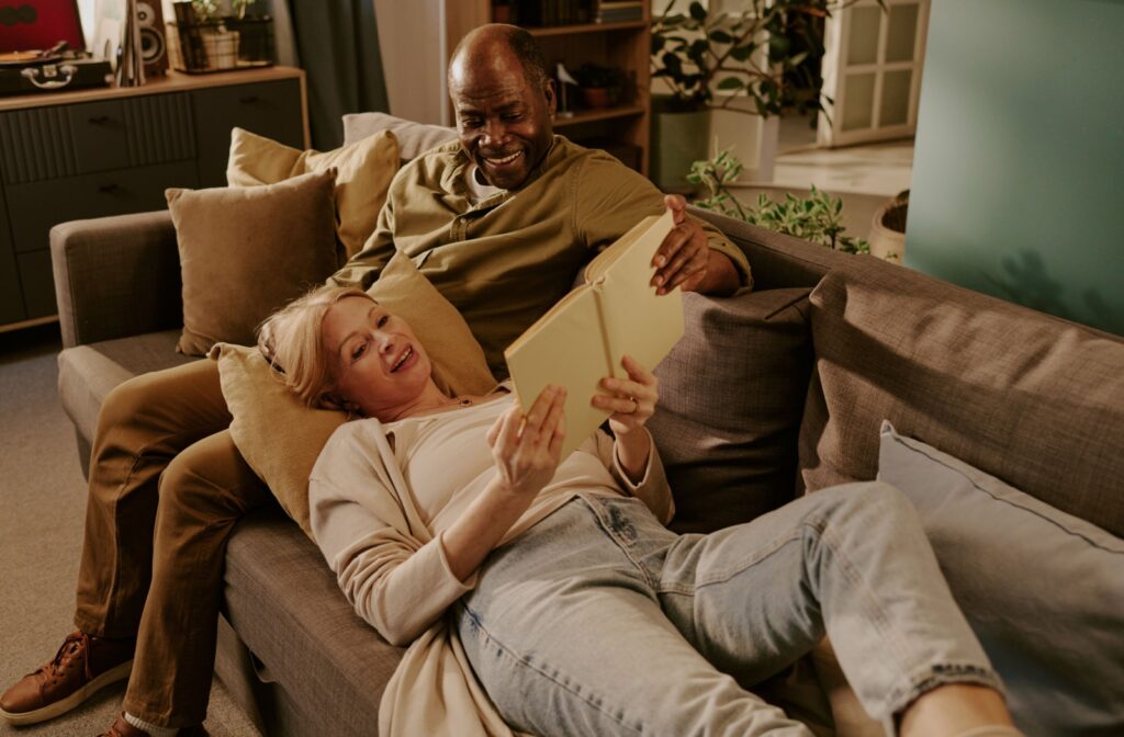 A senior lies with their head on their partner’s lap while reading a book out loud so both parties can enjoy the story