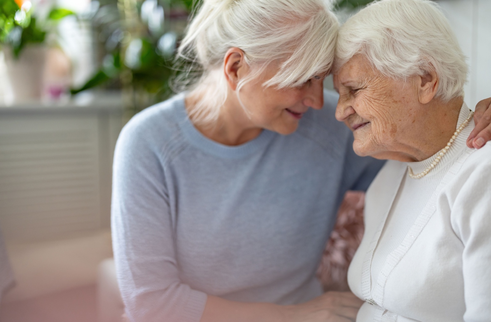 An adult presses their forehead against their older parent’s, providing emotional support on a hard day dealing with dementia