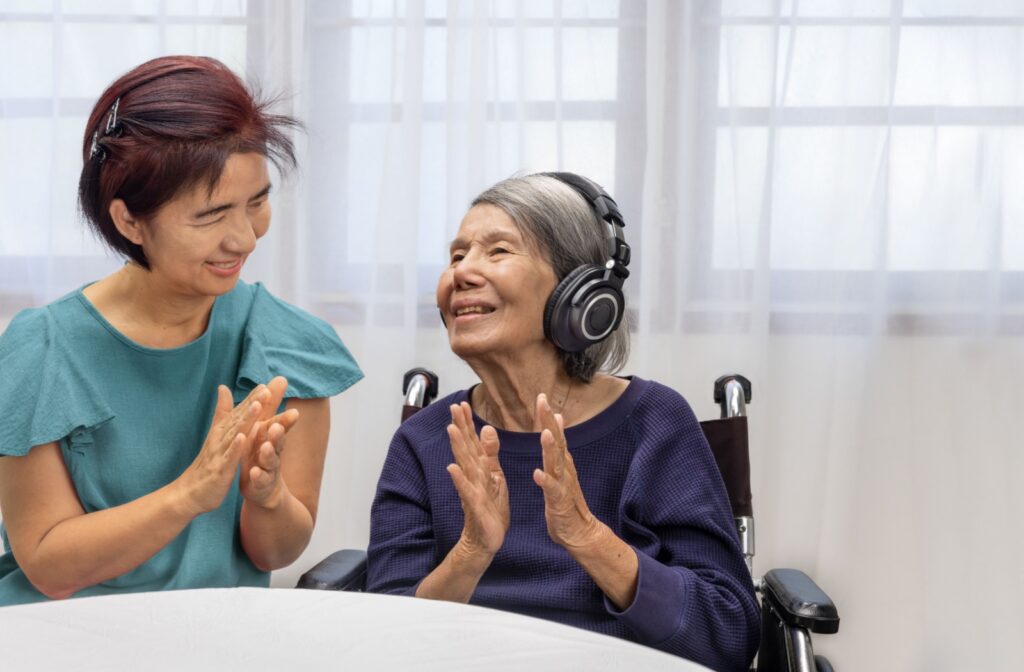 A nurse claps along with a senior listening to music with headphones as a part of music therapy in memory care