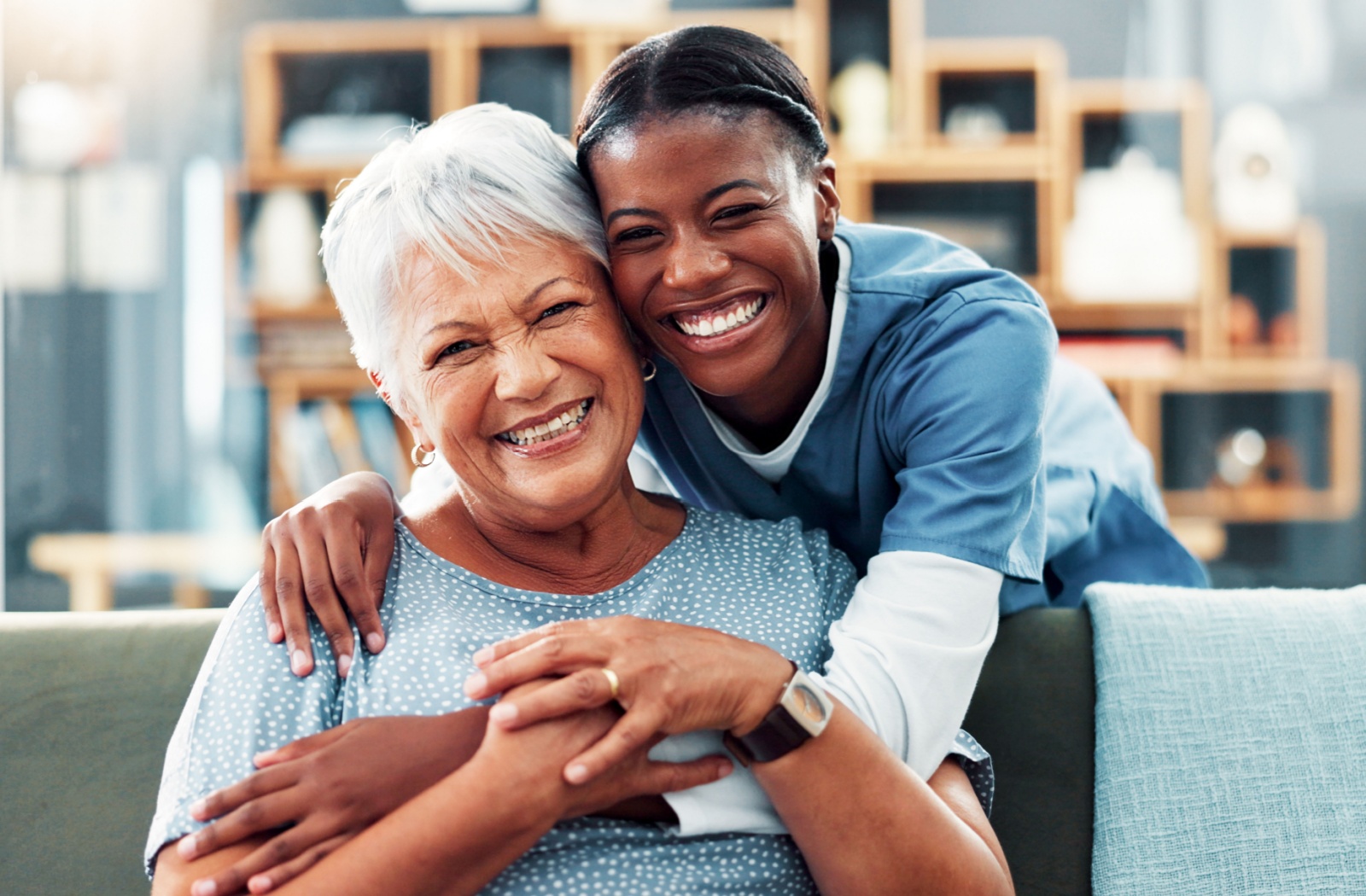 A senior woman and a staff member at an assisted living community hugging each other and smiling.