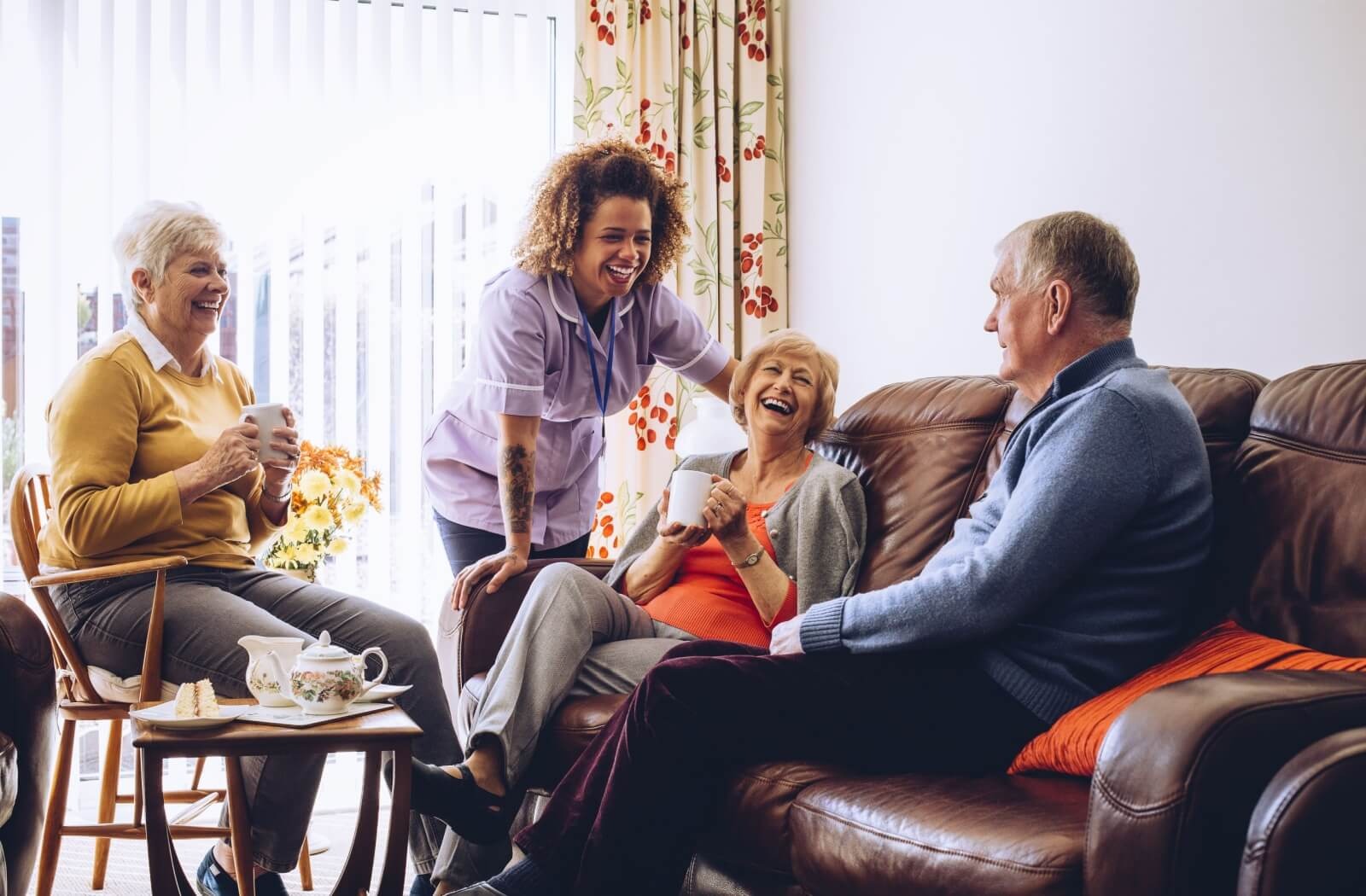 Group of seniors laughing with a team member while sharing tea in a cozy assisted living lounge