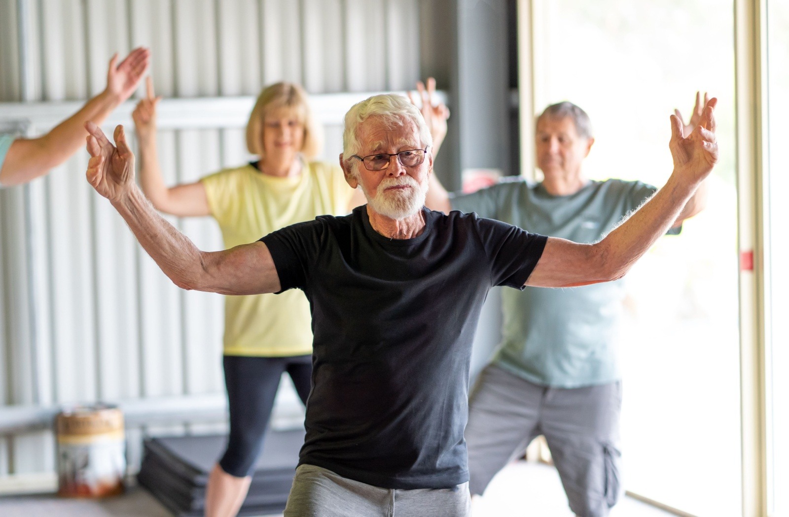A senior raises their arms in a pose during tai chi, a low-impact movement activity.