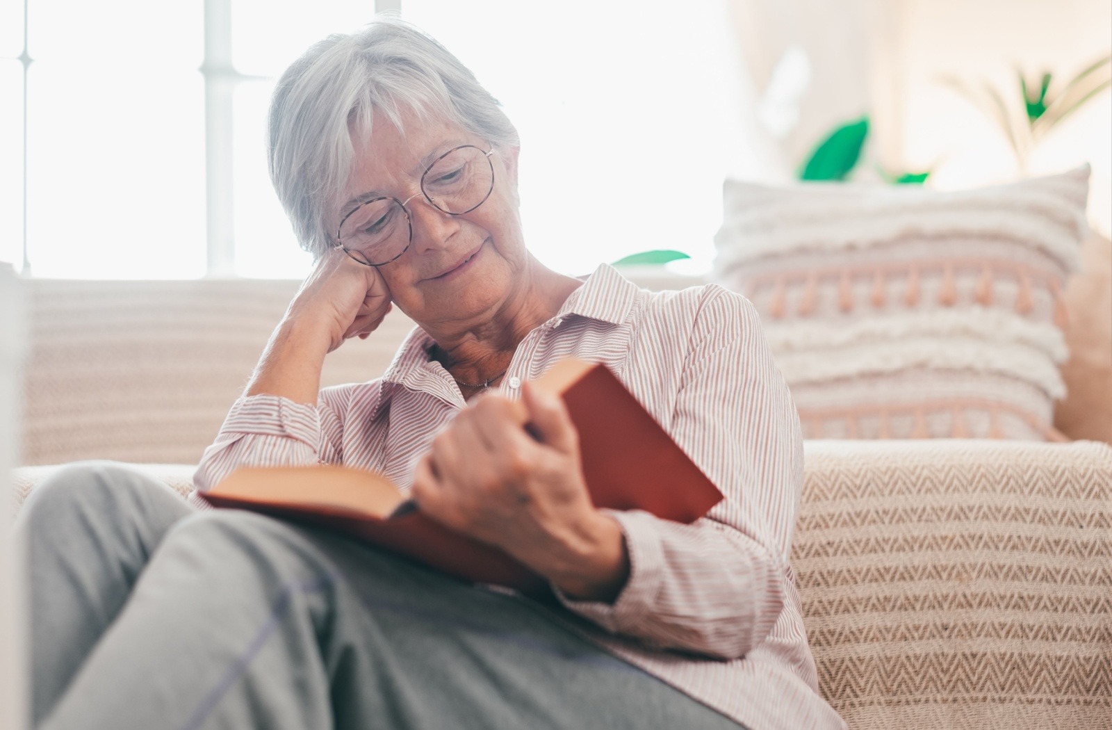 a senior reads a novel while sitting on the floor and leaning against their couch.
